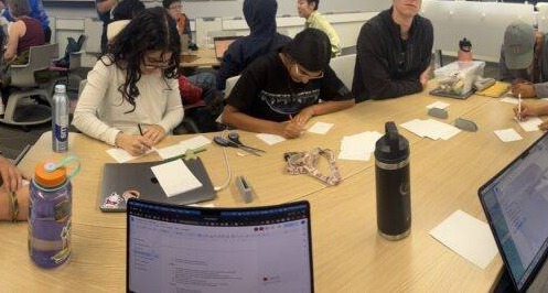 Players writing prompts around a table during a POV playtest in class
